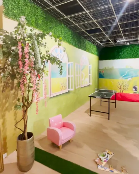 Hoek van het Sprookjesbos met beschilderde raampjes, een roze kinderstoeltje, een bloesemboom en een tafeltennistafel.