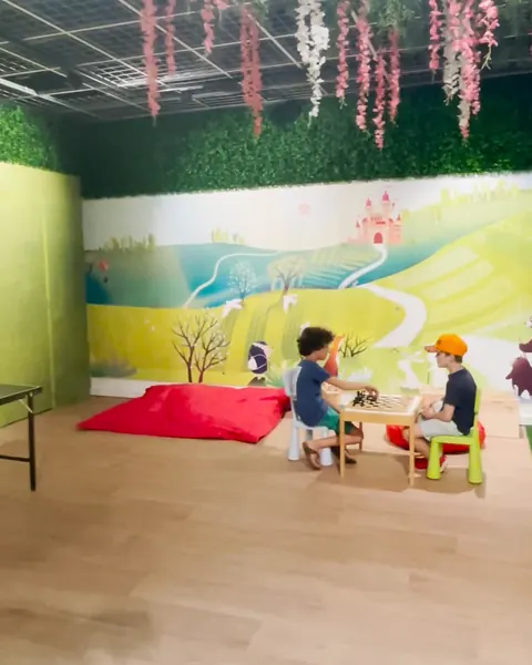 Twee kinderen spelen aan een klein tafeltje in het Sprookjesbos, voor een beschilderde wand met heuvels en een kasteel.